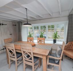 A dining room with a wooden table and six chairs next to a window with three plants York House Thornton Dale