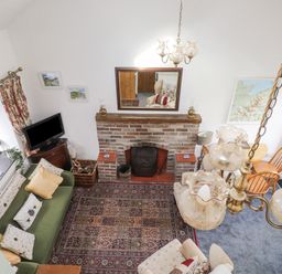 An overhead view of a living room with a brick fireplace a green sofa with cushions a television on a wooden stand a dining table with chairs and a hanging chandelier at Quarry Cottage in Bethesda