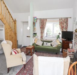 A living room with armchairs a green sofa a brick fireplace TV and window with floral curtains at Quarry Cottage in Bethesda