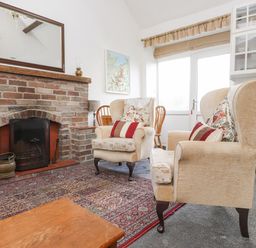 A room with two armchairs a brick fireplace a wooden table and kitchen cabinets at Quarry Cottage in Bethesda