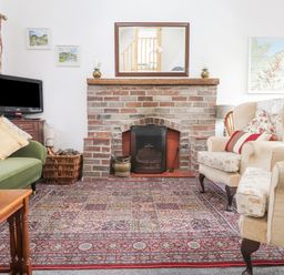 A living room with a brick fireplace two armchairs a green sofa a wooden coffee table a television and framed pictures at Quarry Cottage in Bethesda