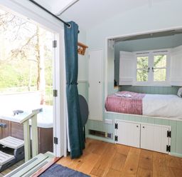 A small room with a bed built into the wall with windows above and a hot tub outside on a wooden deck at Damsel Shepherds Hut in Badwell Ash