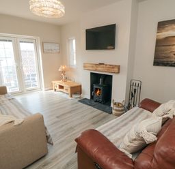 A living room with a beige sofa and a brown leather sofa facing a fireplace with a wood stove and a wall-mounted TV at Ocean Spray in Scarborough
