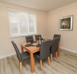 A dining room with a wooden table and six upholstered chairs near a window with blinds at Ocean Spray in Scarborough