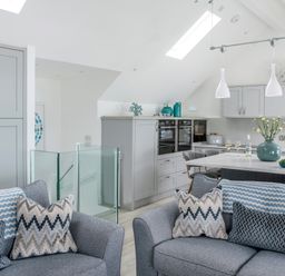 A kitchen and living area with grey sofas with patterned cushions and a kitchen island with flowers at Loe Cottage in Porthleven