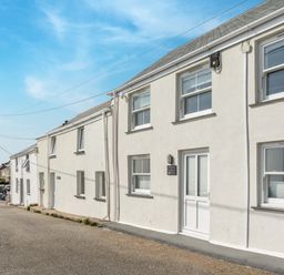 A row of white houses along a street with windows and doors under a clear blue sky at Loe Cottage in Porthleven