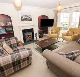 A living room with sofas a coffee table a fireplace a bookshelf and armchairs at The Old Boathouse in Trefin near St Davids