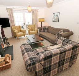 A living room with sofas, armchairs, a coffee table, a fireplace, and a television at The Old Boathouse in Trefin near St Davids