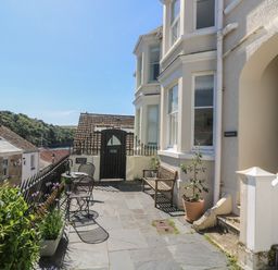 A patio with a metal table and chairs a wooden bench potted plants and a black gate on a stone floor at 21 Passage Street formerly Panacea in Fowey