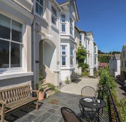 A front patio area with wooden bench metal table and chairs outside white buildings on a street at 21 Passage Street formerly Panacea in Fowey