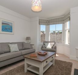 A living room with a grey sofa and armchair a wooden coffee table and bay windows at 21 Passage Street formerly Panacea in Fowey
