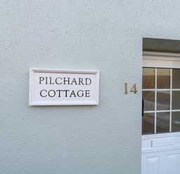 A white door with glass window and house number 14 next to a sign saying Pilchard Cottage in Dawlish
