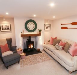 A living room with a sofa, armchair, fireplace, clock, and wooden paddles on the wall at Pilchard Cottage in Dawlish