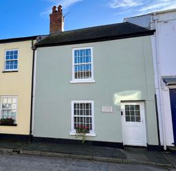 A street view of three attached houses with different colored doors one labeled Pilchard Cottage in Dawlish