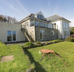 Exterior view of a two-story house with stone and white walls a green lawn and a tree stump in the garden at Lower Mellan Barn in Coverack