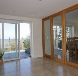 A room with tiled floor sliding glass door leading outside and wooden framed glass doors reflecting a dining area at Lower Mellan Barn in Coverack