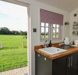 A kitchen with a sink wooden countertop kettle toaster and cups hanging on hooks at Dragonfly Shepherd's Hut Oakford near Aberaeron