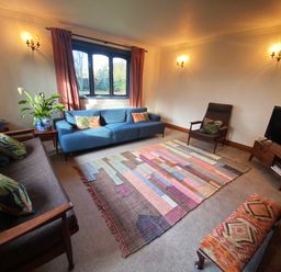 A living room with sofas a chair a TV on a stand and a patterned rug at Rivendell in Weybread near Harleston