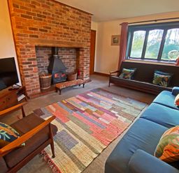 A living room with a brick fireplace wooden chairs sofas a colorful rug and a television at Rivendell in Weybread near Harleston