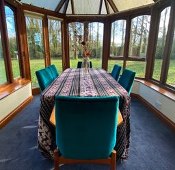 A dining area with a table covered by a patterned cloth and six chairs inside a conservatory at Rivendell Weybread near Harleston