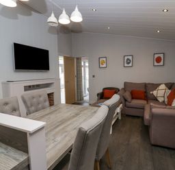 A living room with a dining table chairs sofa and wall mounted TV at The Bothy in Keswick