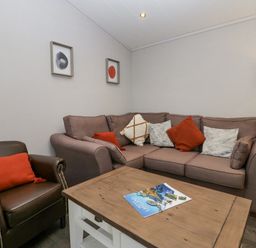 A living room with a brown leather armchair and a beige sofa with cushions a wooden coffee table and floor lamp at The Bothy in Keswick