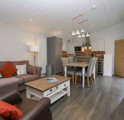 A living area with a sofa and armchair a wooden coffee table and a dining table with four chairs near a kitchen at The Bothy in Keswick