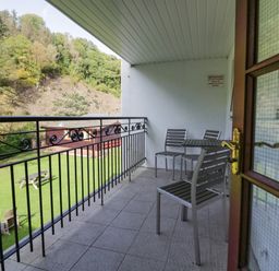 A balcony with metal chairs and table overlooking a lawn with wooden benches and trees at Apartment 1 in Keswick