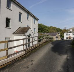 A paved road leading up to multiple white buildings with a wooden fence on the left and trees in the background at Apartment 4 in Keswick