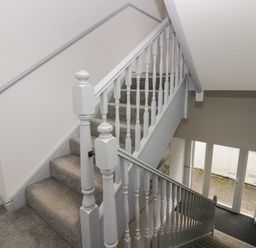 A carpeted staircase with white wooden banisters and handrails leading downstairs to a glass door entrance in Apartment 6 Keswick
