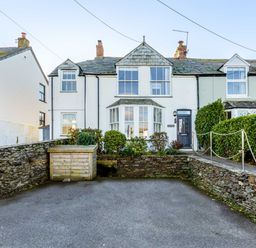 A front view of a white terraced house with bay windows stone walls and a paved driveway at Tre Lowen in Port Isaac