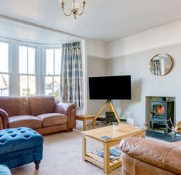 A living room with brown leather sofas a blue ottoman wooden coffee table a television on a wooden tripod stand and a fireplace at Tre Lowen in Port Isaac