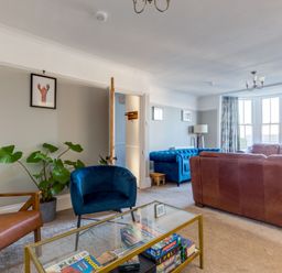A living room with a glass coffee table holding board games two armchairs a leather sofa and a large window with curtains at Tre Lowen in Port Isaac