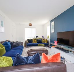 A living room with blue and green cushions on sofas and a television on a stand at Cobalt in St Eval near Mawgan Porth