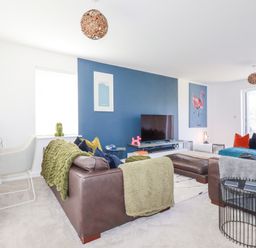 A living room with blue accent wall a television brown leather sofas and colorful cushions at Cobalt in St Eval near Mawgan Porth