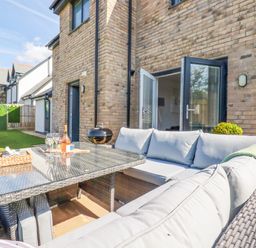 An outdoor patio area with cushioned wicker seating and a glass-top table next to a brick house at Cobalt in St Eval near Mawgan Porth
