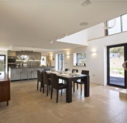 A dining area with a table set for six and an open kitchen with bar stools at The Milking Shed in Bantham