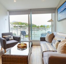 A living room with a sofa armchair glass coffee table and a balcony overlooking a marina at Sea Breeze in Porthmadog