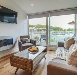 A living room with a sofa chairs coffee table wall-mounted tv and glass door overlooking a marina at Sea Breeze in Porthmadog
