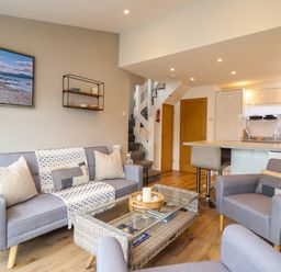 A living room with sofas, a wicker coffee table, kitchen area, and stairs at Sea Breeze in Porthmadog