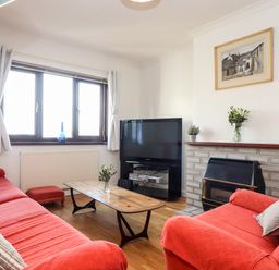 A living room with red covered sofas a wooden coffee table a television and a fireplace at Chi an Vre in Newlyn