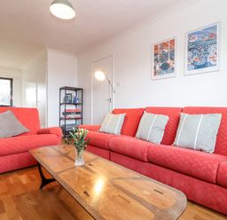 A living room with red sofas a wooden coffee table with flowers on it a black shelving unit and framed pictures on the wall at Chi an Vre in Newlyn