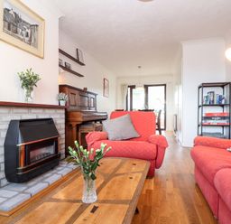 A living room with red sofas a wooden coffee table a fireplace a piano and shelves at Chi an Vre in Newlyn