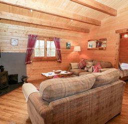 A living room with couches a wood burning stove and a doorway leading to a bedroom at Ballinorig Lodge in Cleator Moor