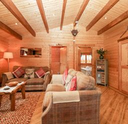 A wooden living room with two sofas a coffee table a floor lamp and a cabinet with flowers at Ballinorig Lodge in Cleator Moor