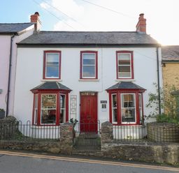 Exterior of a two story house with red door and window frames and a small front garden at Ty Len in St Davids