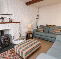 A living room with a fireplace two sofas colorful cushions and a patterned ottoman at Ty Len in St Davids