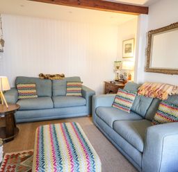 A living room with two blue sofas patterned cushions an ottoman wooden side table with a lamp and a large mirror on the wall at Ty Len in St Davids