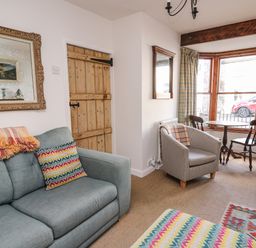 A sitting room with a blue sofa, armchair, wooden table with two chairs by a bay window, and a television at Ty Len in St Davids
