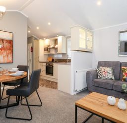 An open plan living room and kitchen with a dining table set and a grey sofa with cushions at Squirrels Nook Waterside Wood 19 White Cross Bay near Windermere